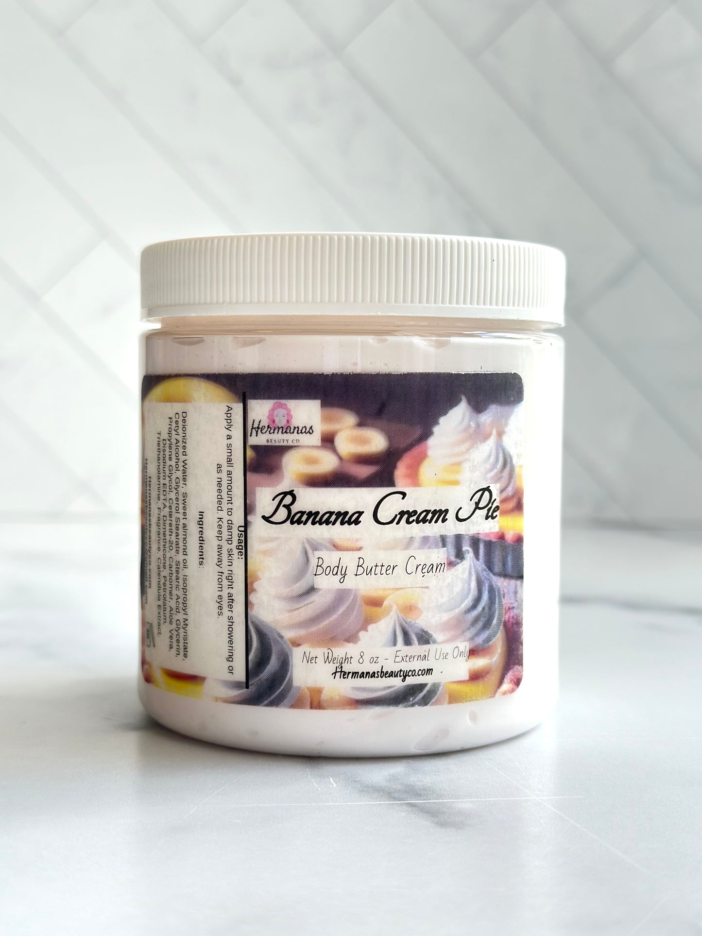 Clear body butter jar with white lid and a label showing a banana cream pie, the name of the product and the size