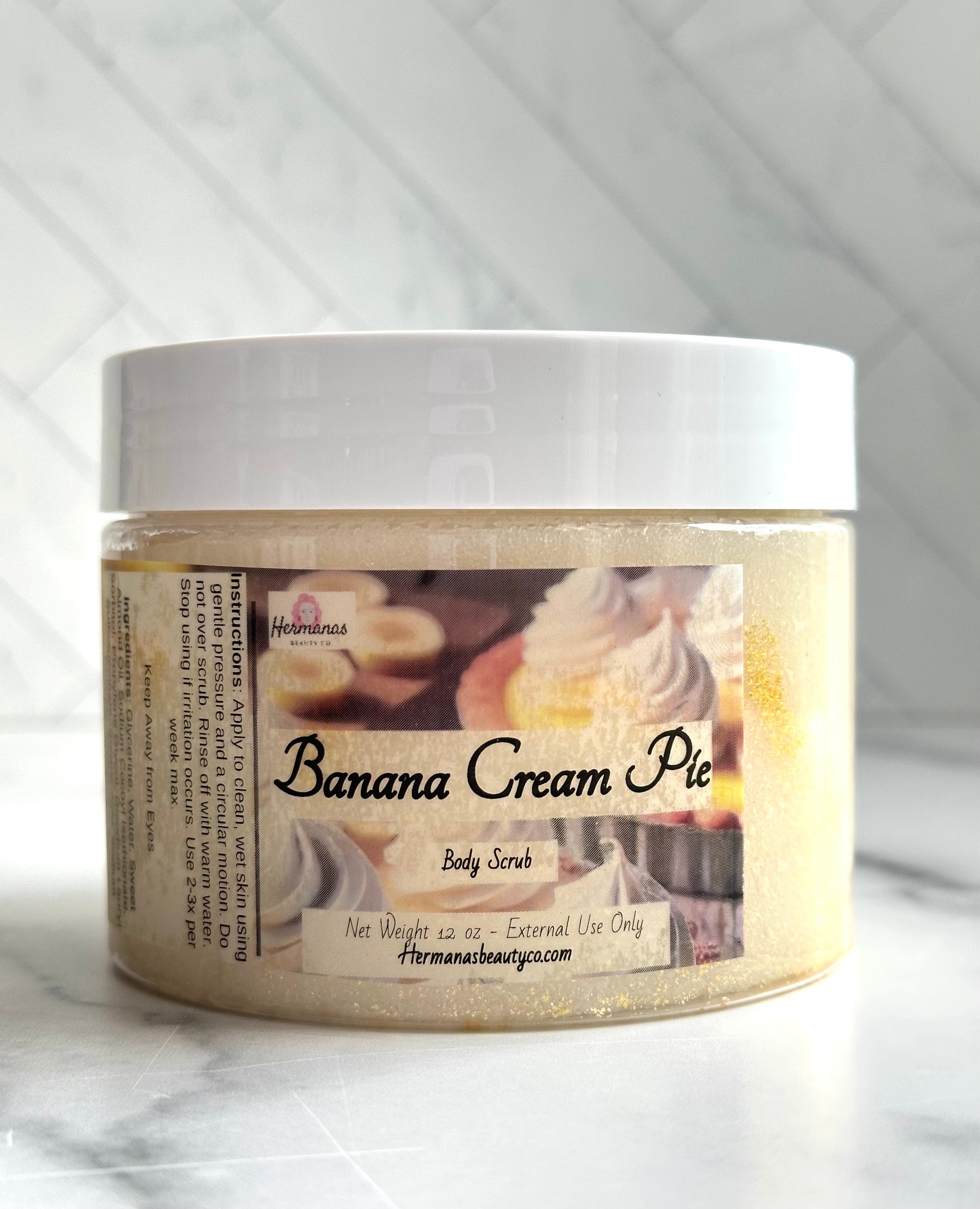 Clear body scrub jar with white lid and a label showing a banana cream pie, the name of the product and the size