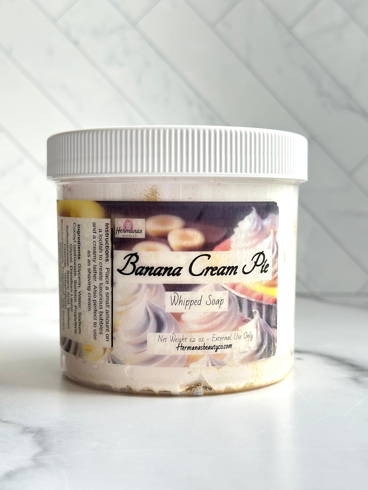Clear whipped soap jar with white lid and a label showing a banana cream pie, the name of the product and the size