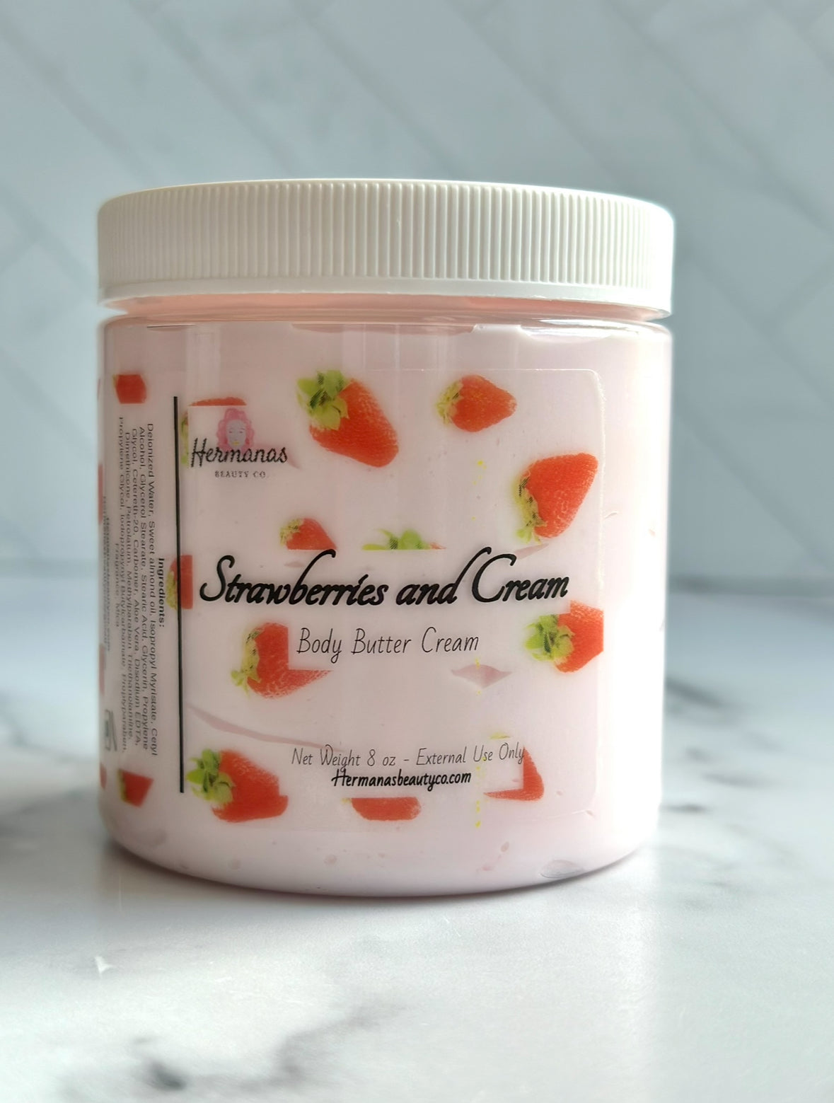 Jar of 'Strawberries and Cream' body butter cream on a marble surface with a light gray background