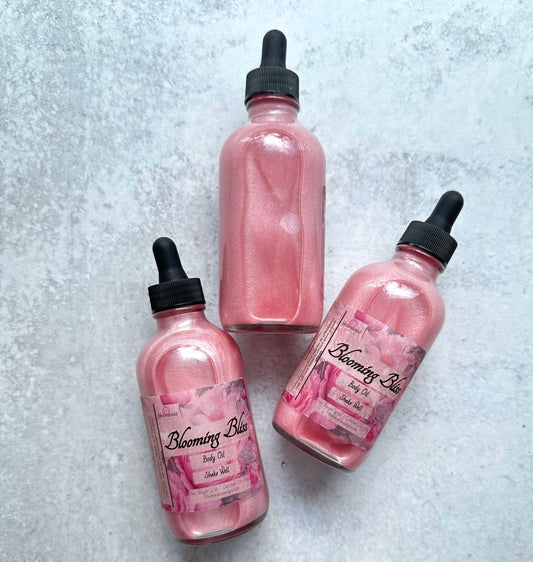 Clear bottles with pink sparkling body oil inside. Labels are colorful and pink. The bottle tops are black.