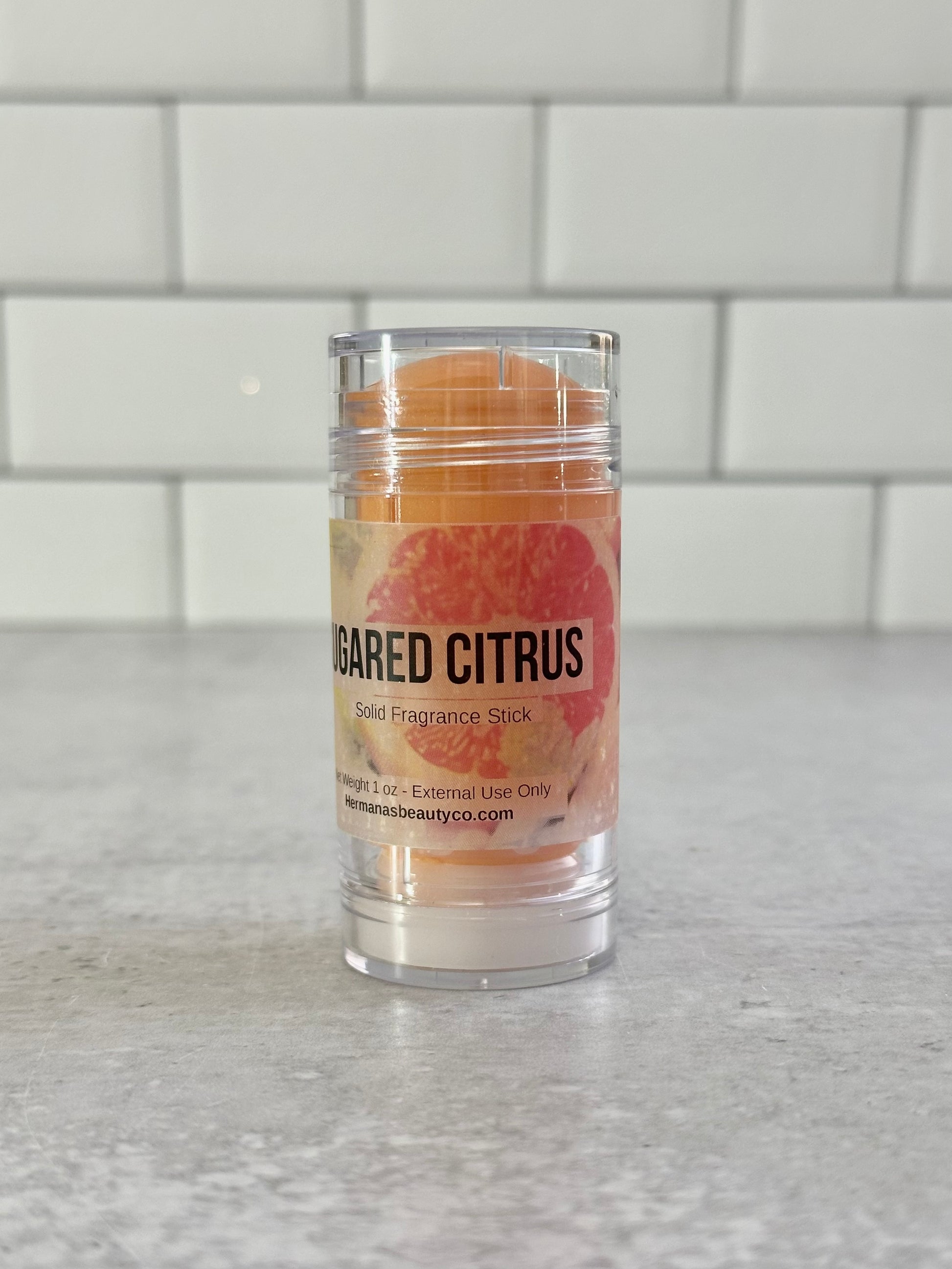 Solid perfume Bar in a clear container on a gray surface with a white tiled wall background