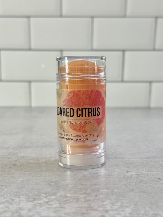 Solid perfume Bar in a clear container on a gray surface with a white tiled wall background