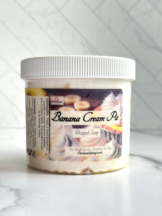 Clear whipped soap jar with white lid and a label showing a banana cream pie, the name of the product and the size 