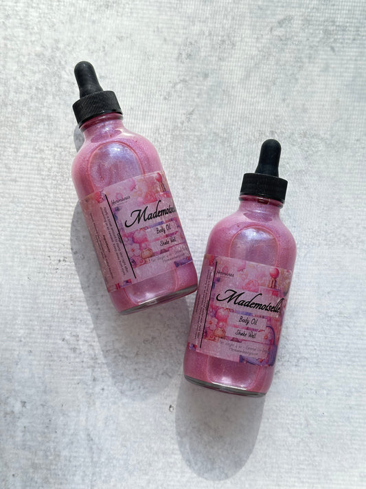 Clear bottles with pink sparkling body oil inside. Labels are colorful and pink. The bottle tops are black.