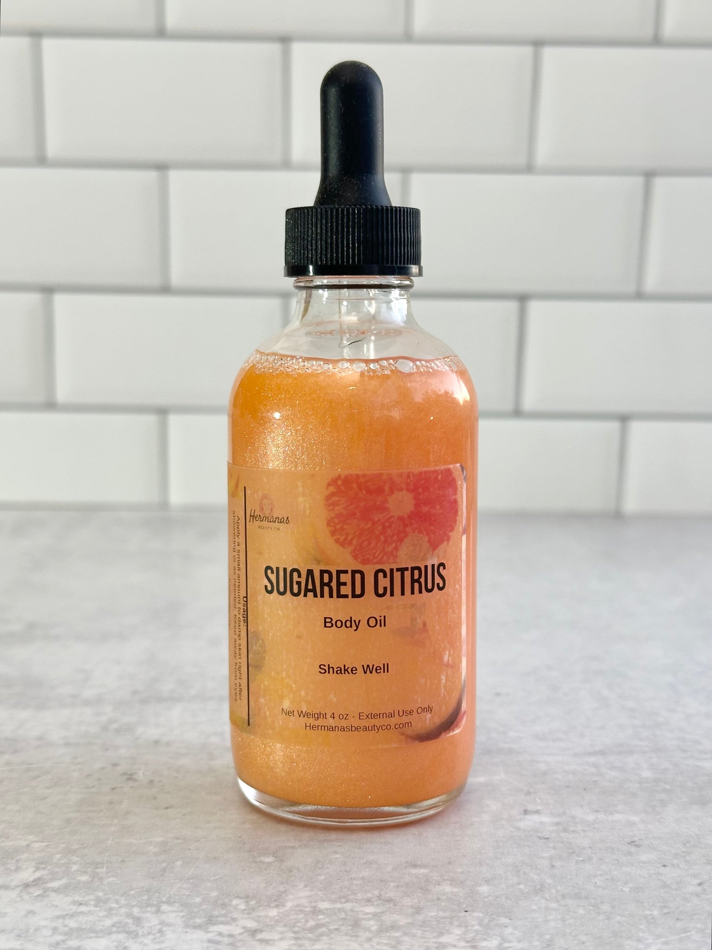 Bottle of Sugared Citrus body oil on a white countertop with a tiled wall background
