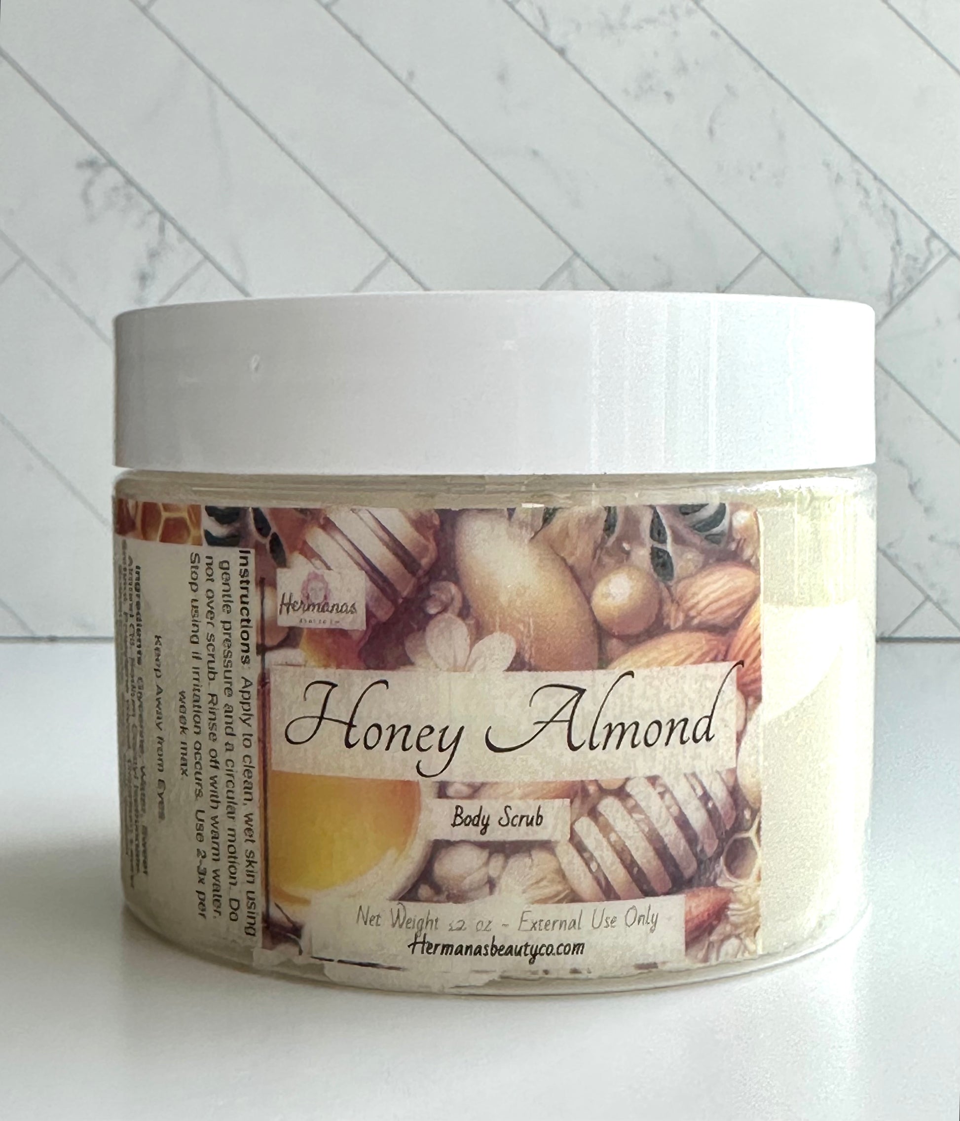 Clear Body scrub jar with a gold and brown label that has the name of the scrub, bees, honey and almonds on it