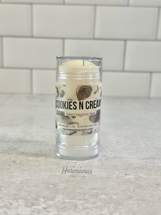Cookies N Cream solid fragrance stick in a clear container on a light gray surface with a tiled wall background.