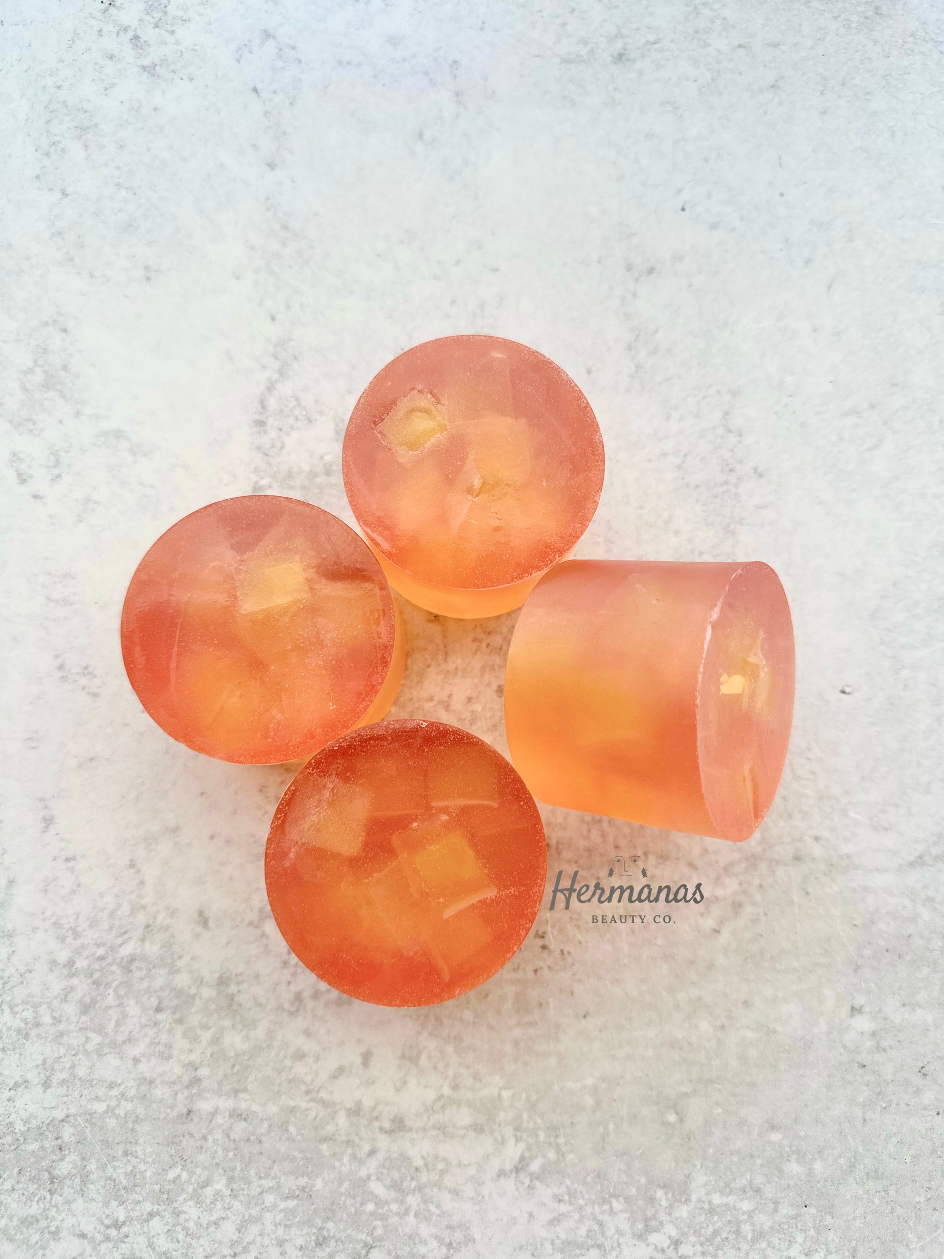 Four pink lemonade themed soap bars on a textured white surface with 'Hermanas Beauty Co.' branding.
