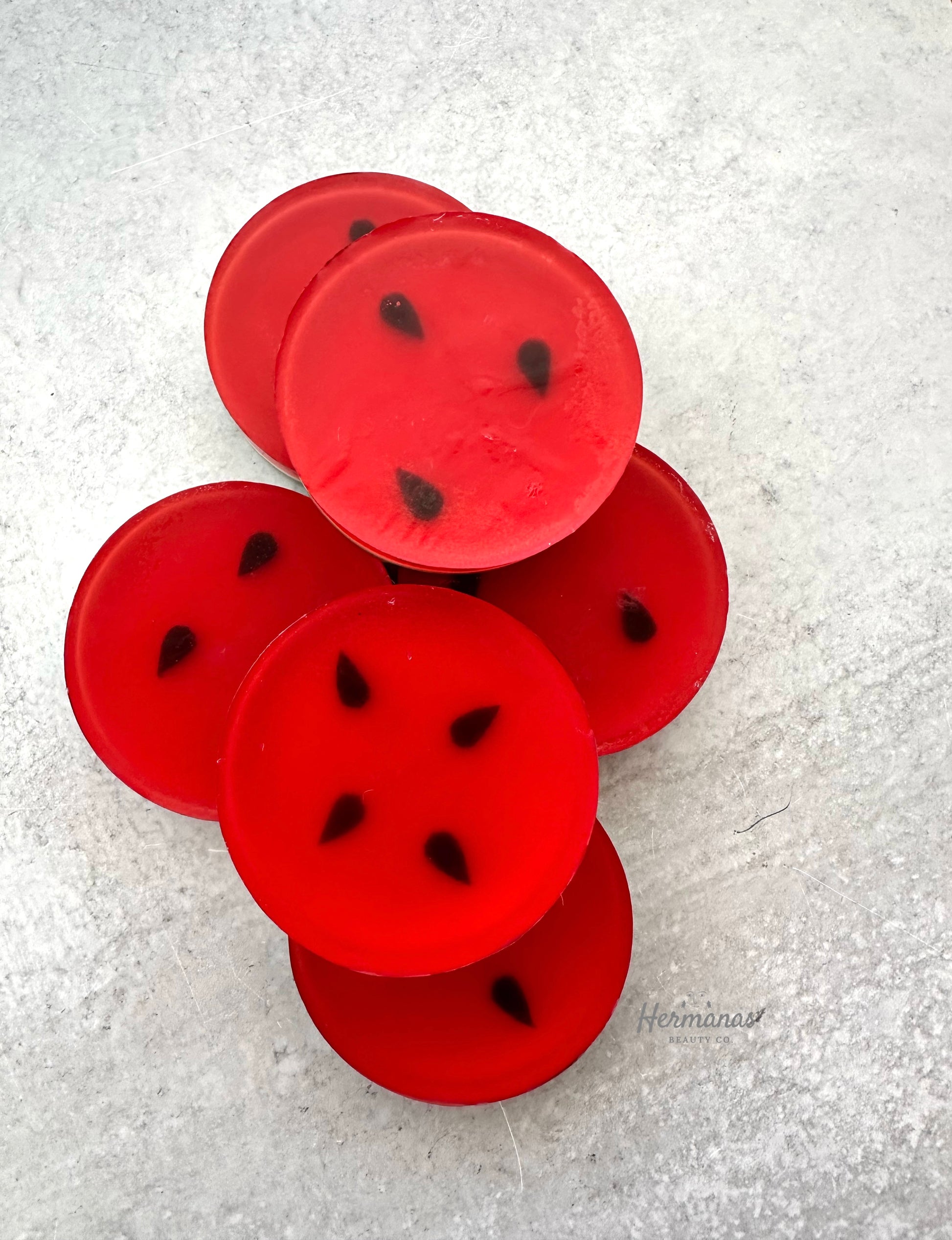 Red watermelon-shaped objects with black seeds on a textured white surface