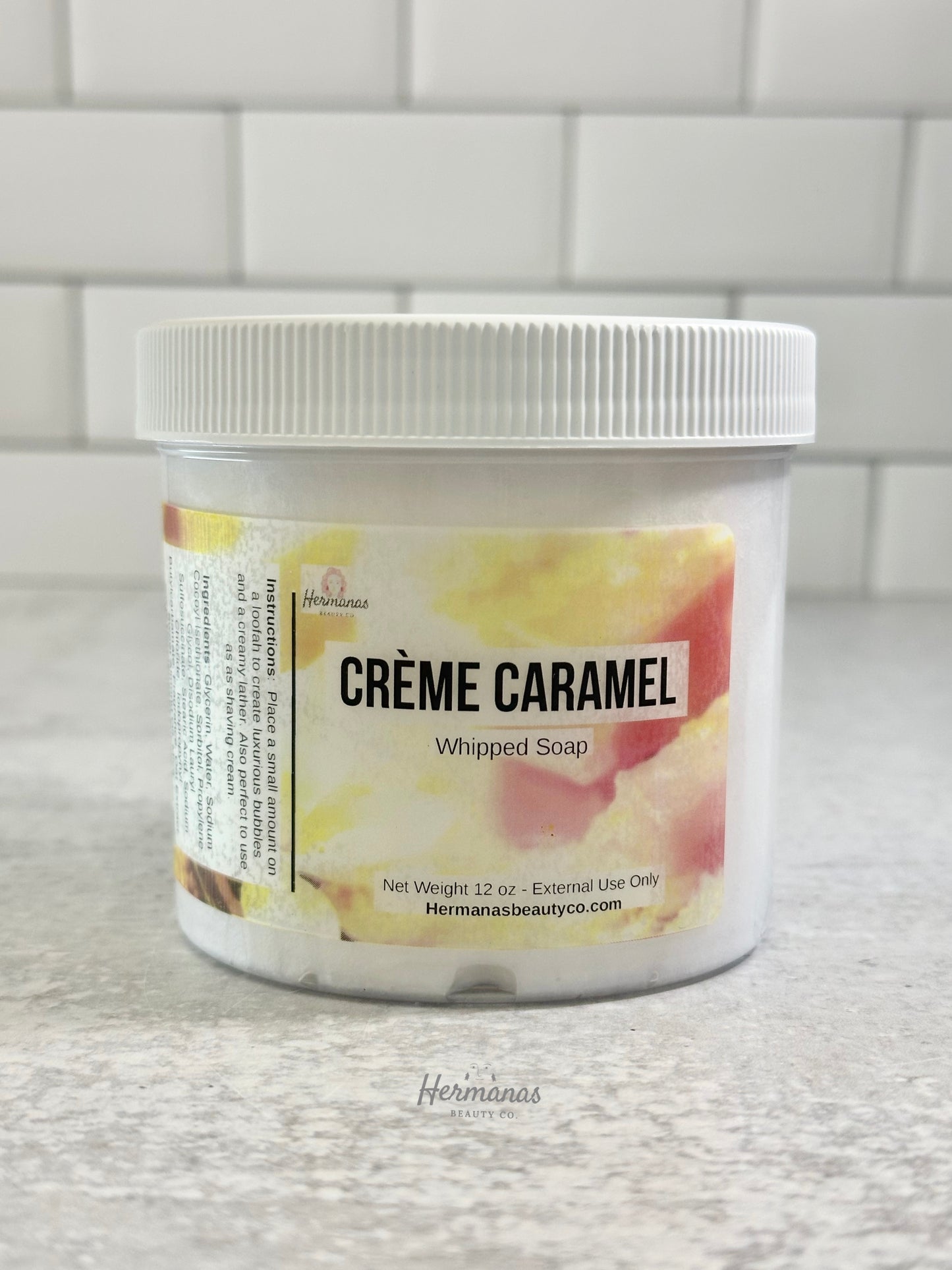 Jar of 'Creme Caramel' whipped soap with a white lid on a tiled bathroom floor.
