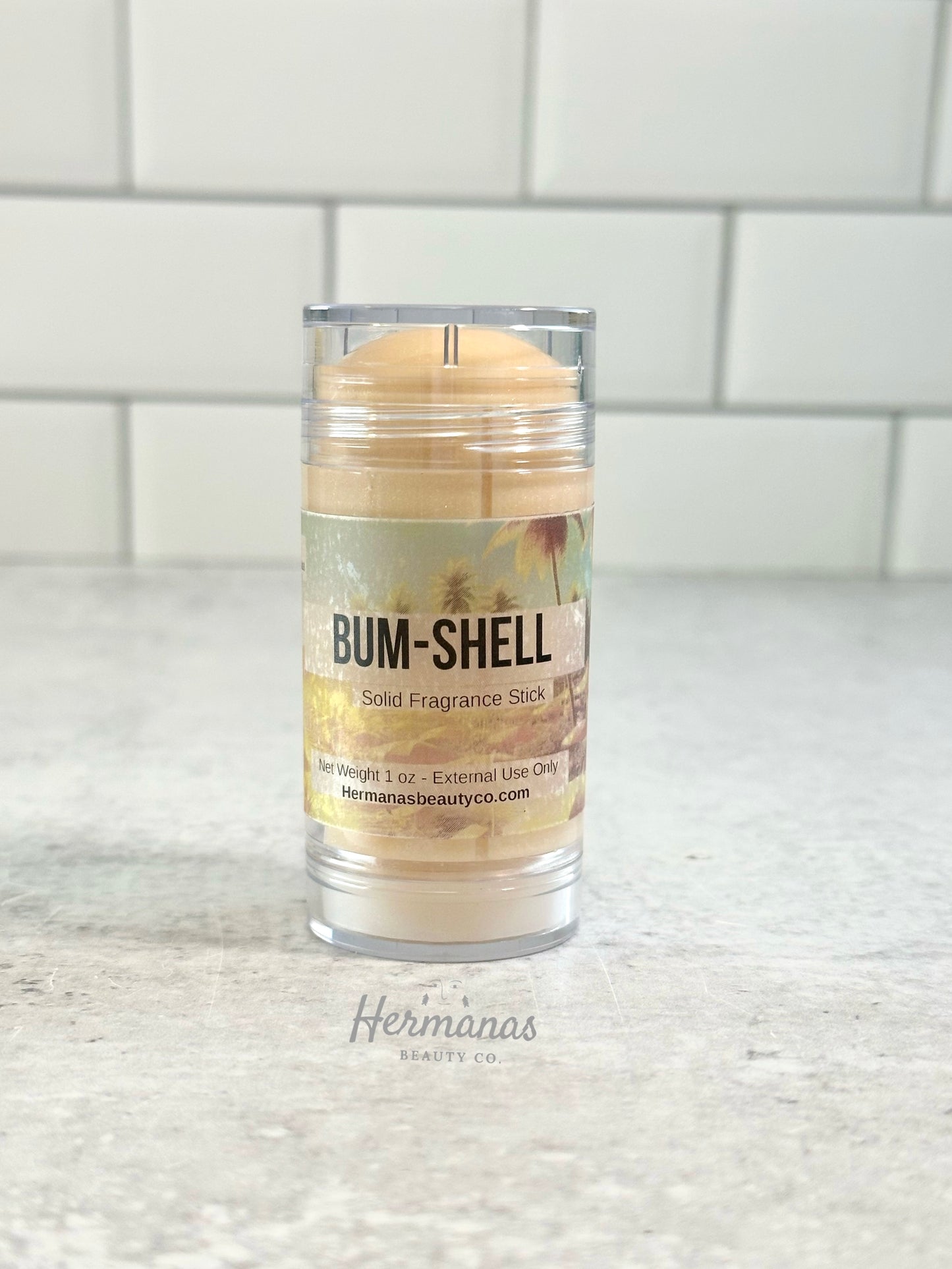 Solid fragrance stick in a clear container with 'Bum-Shell' label on a white surface.