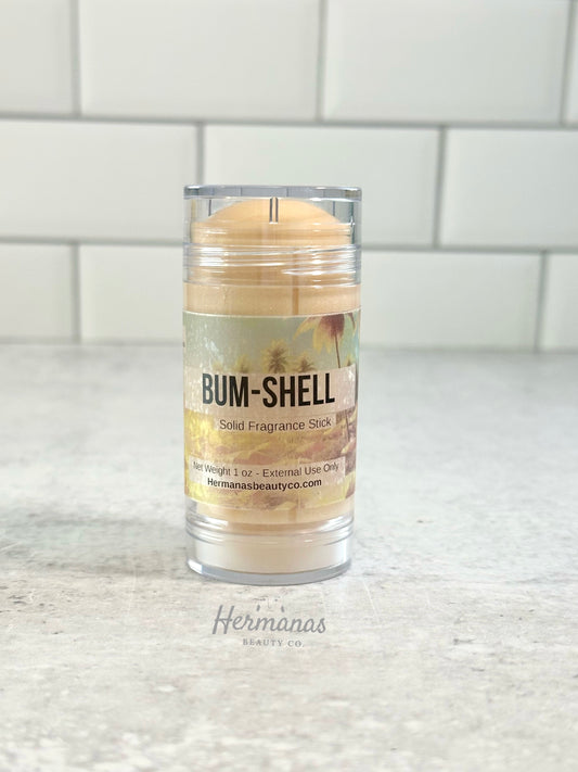 Solid fragrance stick in a clear container with 'Bum-Shell' label on a white surface.