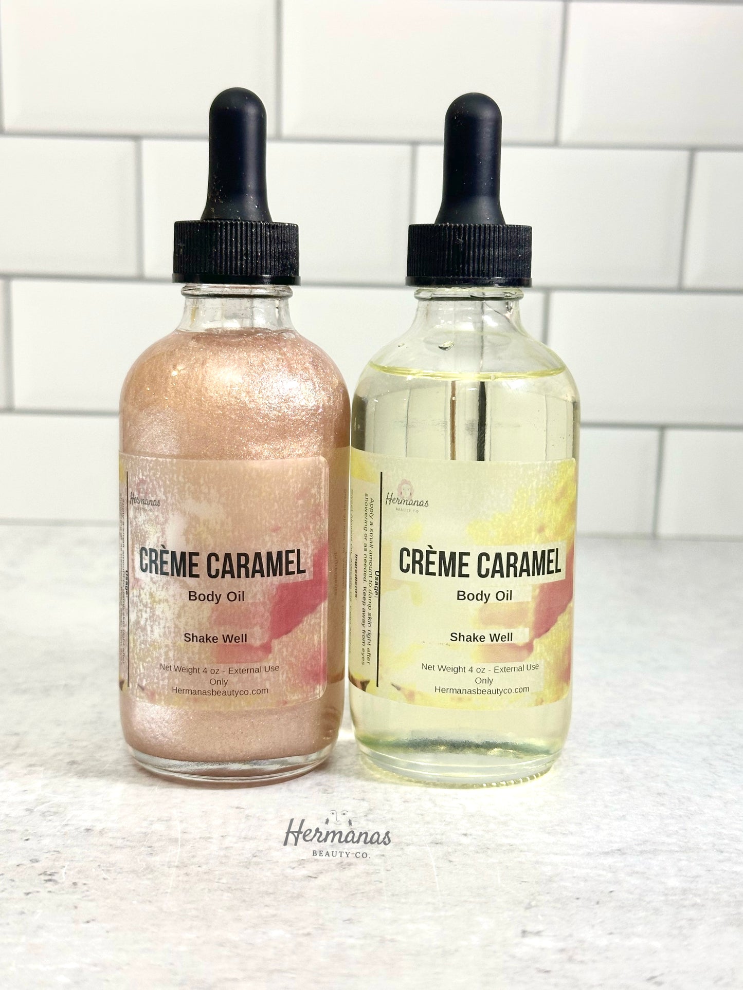 Two bottles of 'Cèreme Caramel' body oil on a white surface with a tiled wall background.