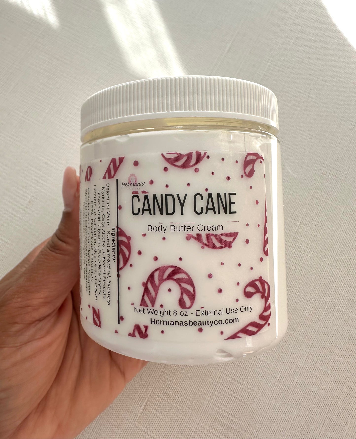 Jar of Candy Cane body butter cream held by a hand on a neutral background