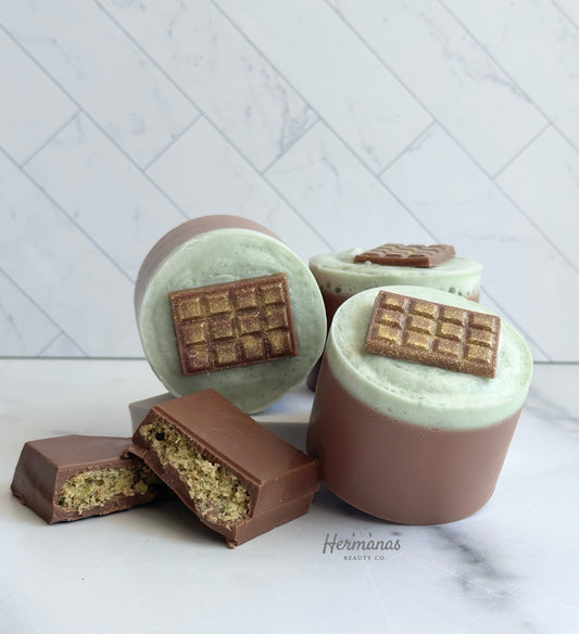 Round brown soap bar with green foamy topping and a soap mini chocolate bar on top that is dusted with gold