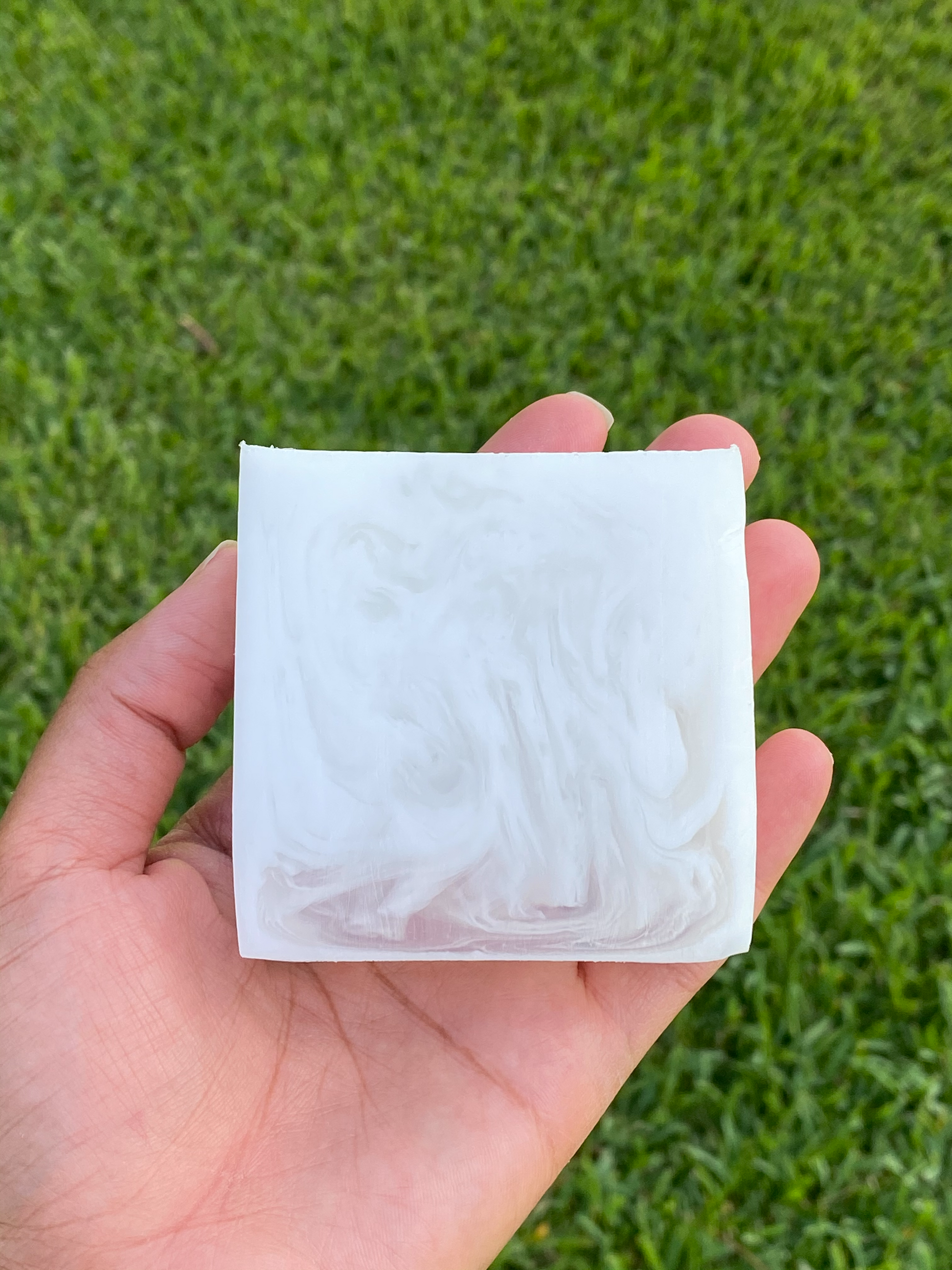 White and clear bar of soap. There is a hand holding the soap and there’s a green background.